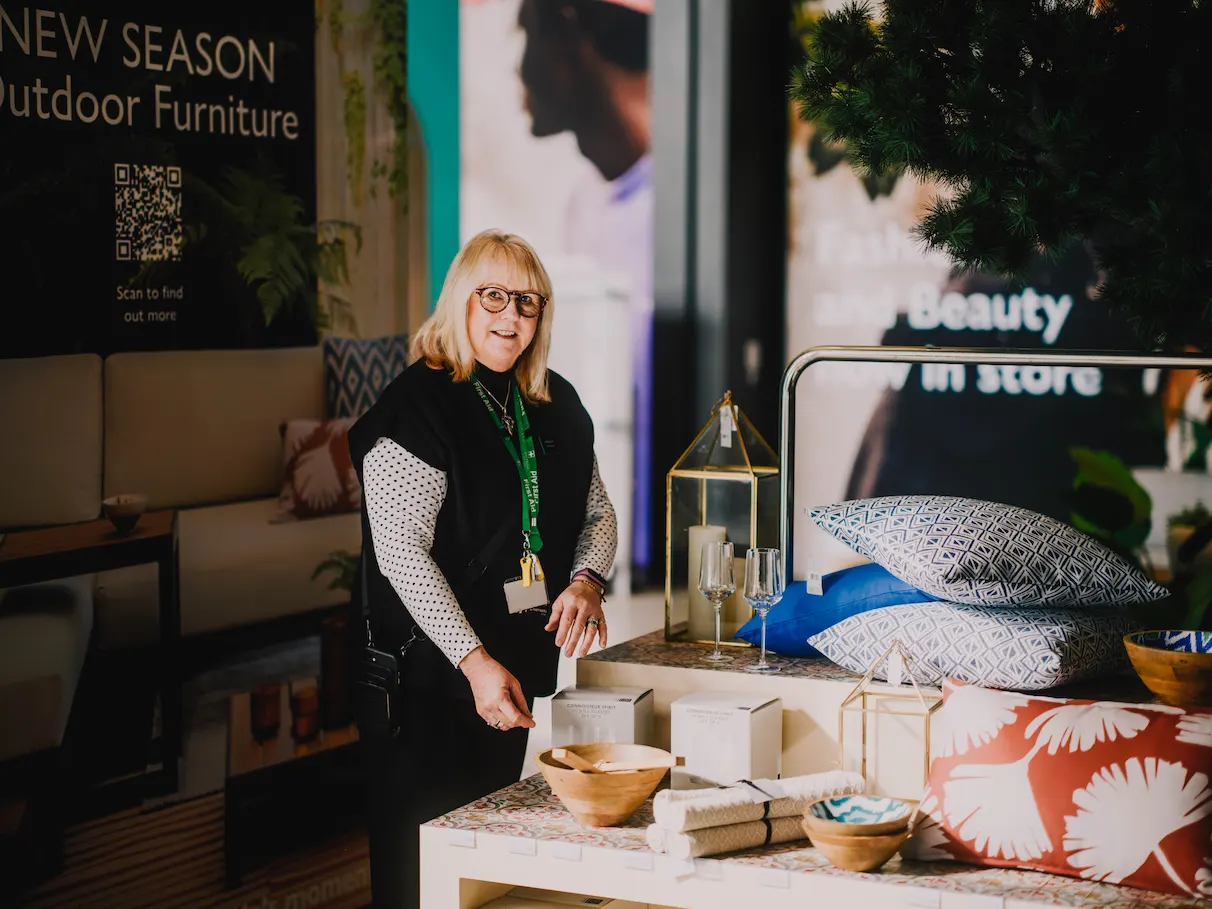 Female John Lewis partner organising items on a display table whilst looking at camera.
