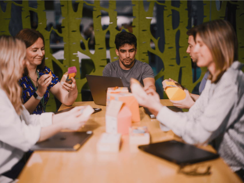 A group of John Lewis employees in a meeting looking at laptops and phones.