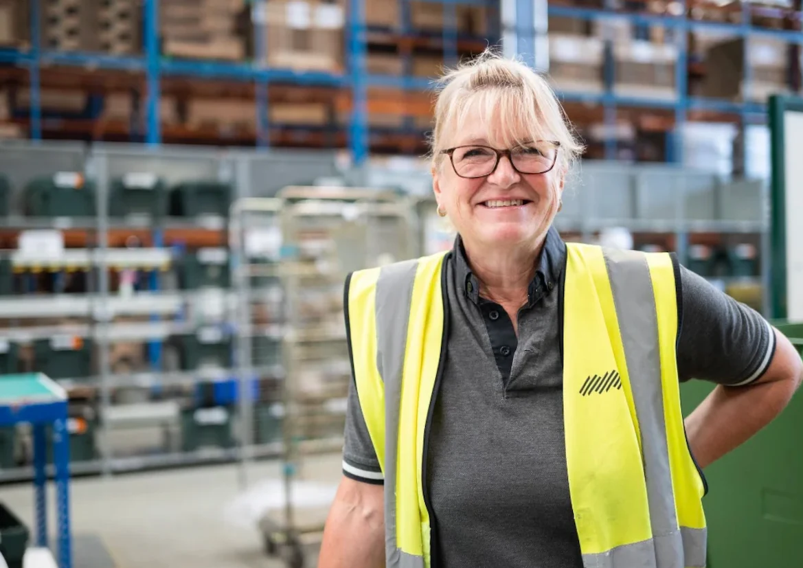 Woman in high-vis jacket smiling at camera on Warehouse floor