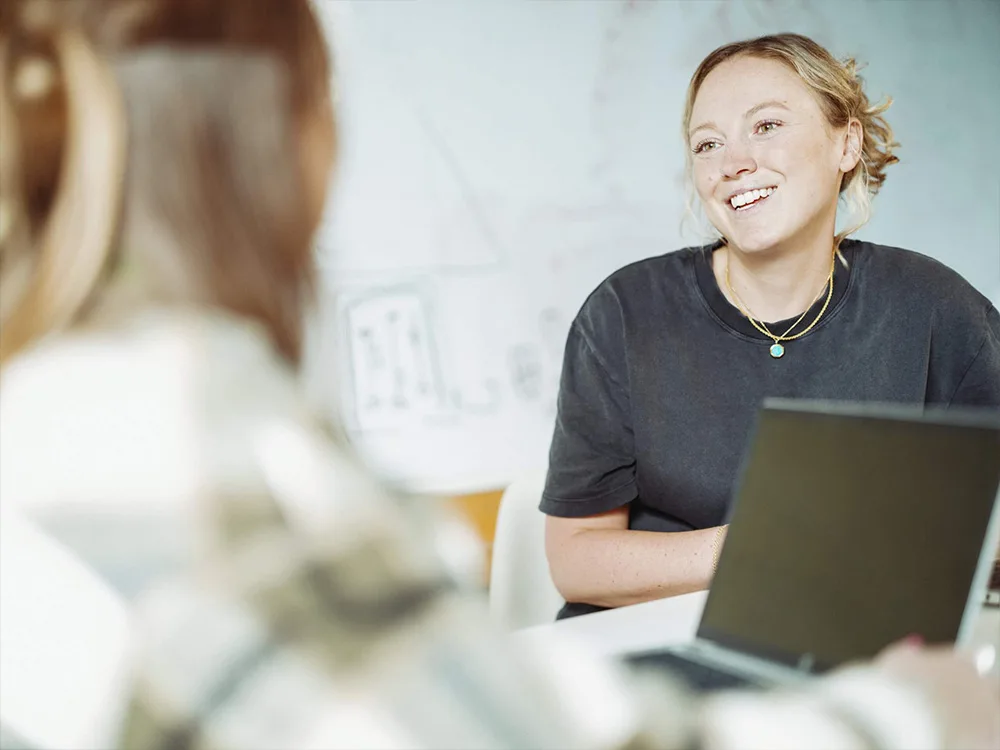 Two female John Lewis employees smiling in front of laptops in meeting