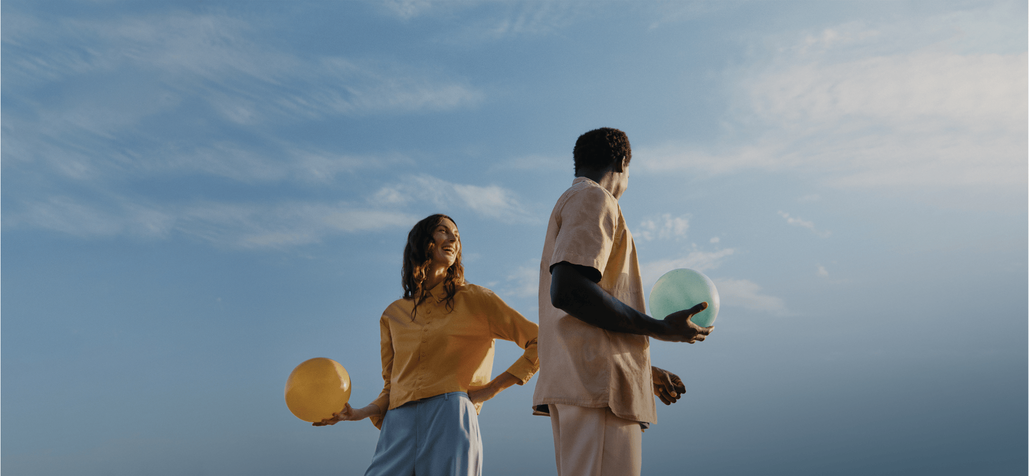 Two people looking at each other laughing and holding a balloons. A nice summer sky in the background.