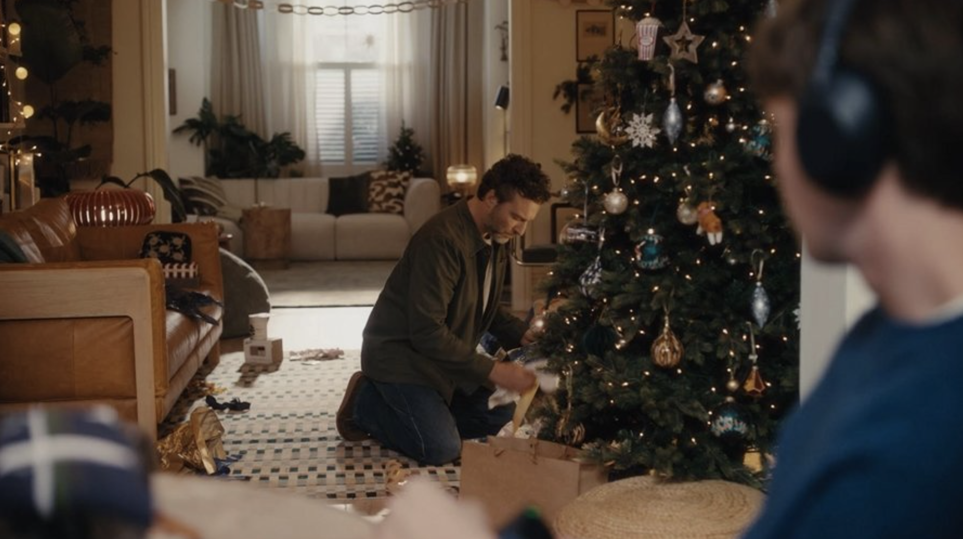 Image from the advert of a Dad finding a gift wrapped under the Christmas tree with his son looking on